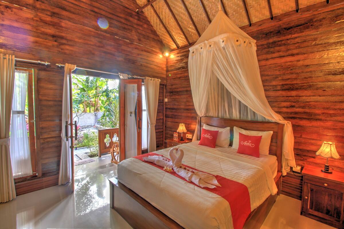 A wooden room with a bed, a nightstand, and a window with curtains.