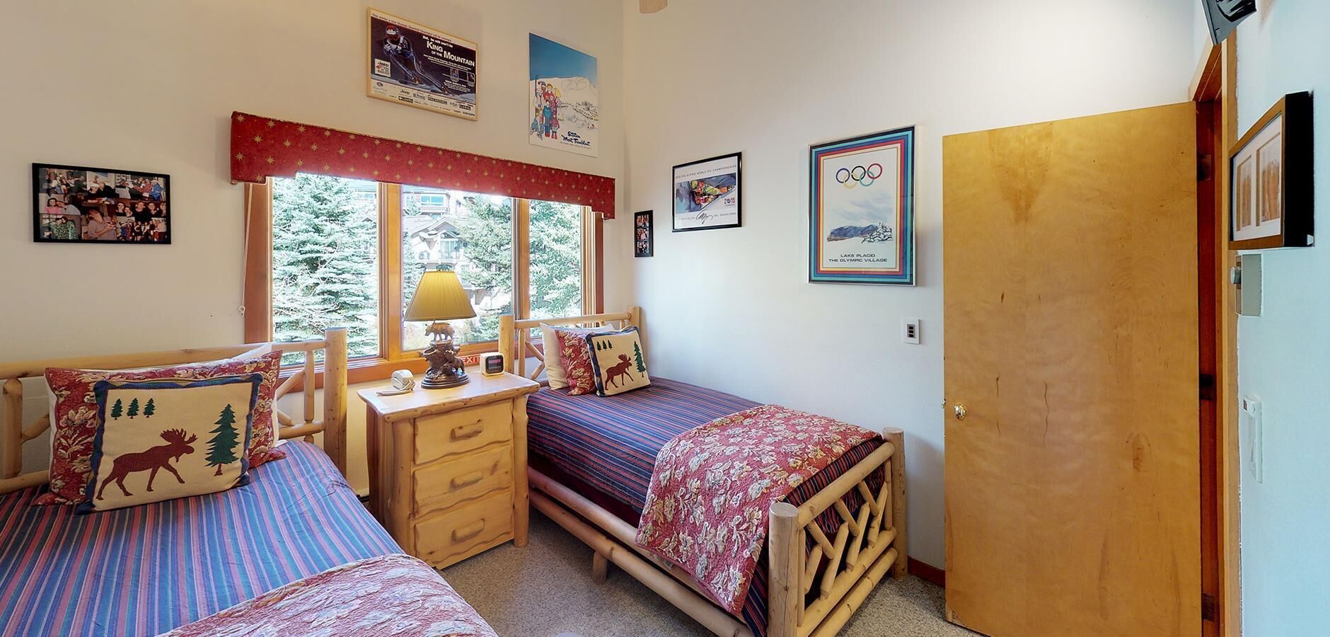 A cozy bedroom with two beds, a wooden dresser, and a window with a view of trees.