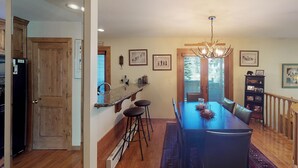A spacious dining area with a long table, bar stools, and a chandelier. - Elegant Creekside Condo with Scenic Views & Pool with Access to Grand Hyatt (Vail)