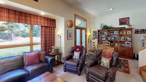A cozy living room with leather furniture, a fireplace, and a bookshelf filled with framed photos and books. - Elegant Creekside Condo with Scenic Views & Pool with Access to Grand Hyatt (Vail)