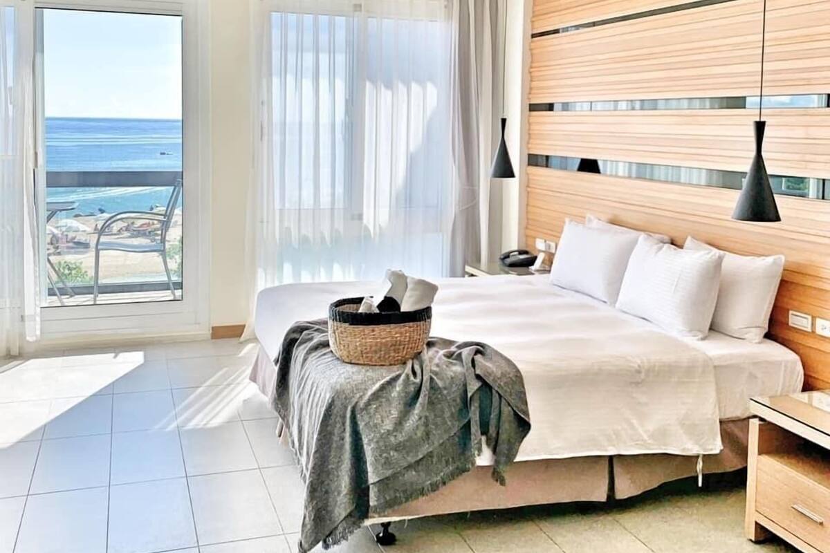 A hotel room with a bed, bedside table, and a view of the beach.