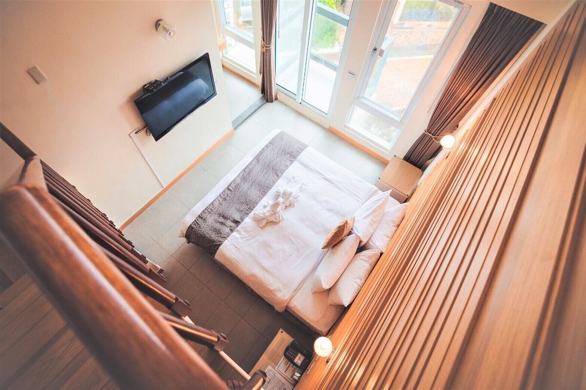 A bedroom with a bed, a TV mounted on the wall, and a view of the outdoors through a sliding door.