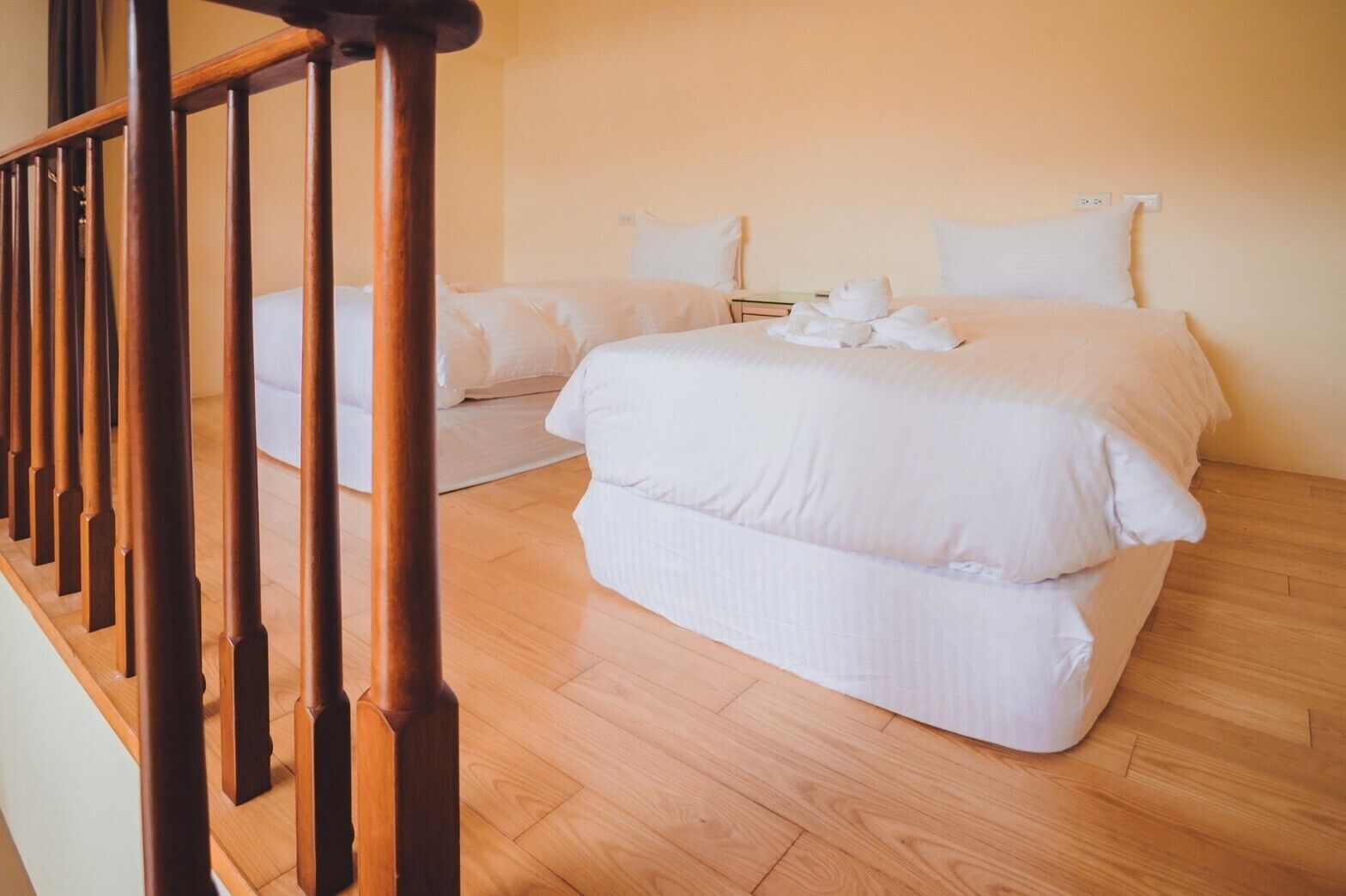 Una habitación de hotel con escalera de madera, una cama grande con ropa blanca y piso de madera.