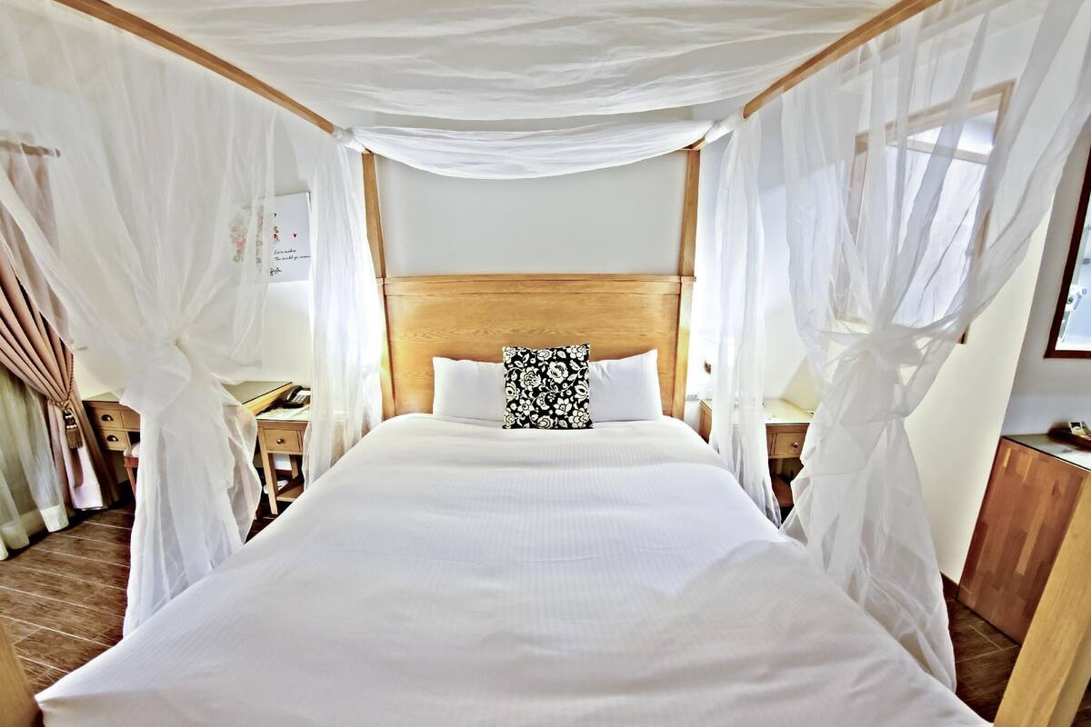 A bed with white linens and a wooden headboard, surrounded by sheer white curtains.