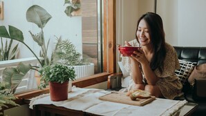 A person sitting on a couch with a bowl of food, a cutting board with a knife, and a potted plant on a table. - Sasalamo (Hengchun)