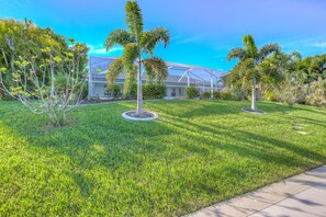 Stroll through the beautifully landscaped garden, surrounded by lush greenery and palm trees, to the modern building with large windows.