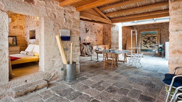 Un intérieur rustique avec des murs en pierre, un plafond en bois, un lit, une table à manger et un grand tableau.