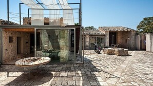 Une cour dallée de pierres, une structure à ossature de verre et des bâtiments traditionnels aux toits de tuiles.