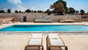 Une piscine avec des chaises longues et un mur de pierre en arrière-plan.