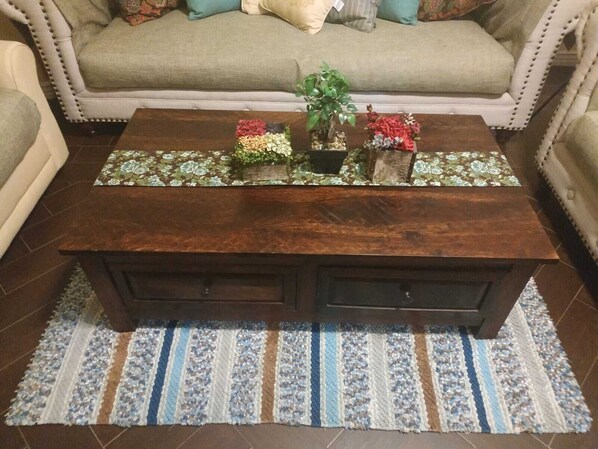 Una mesa de centro de madera con un camino de mesa estampado con motivos florales, una planta en maceta y flores decorativas.