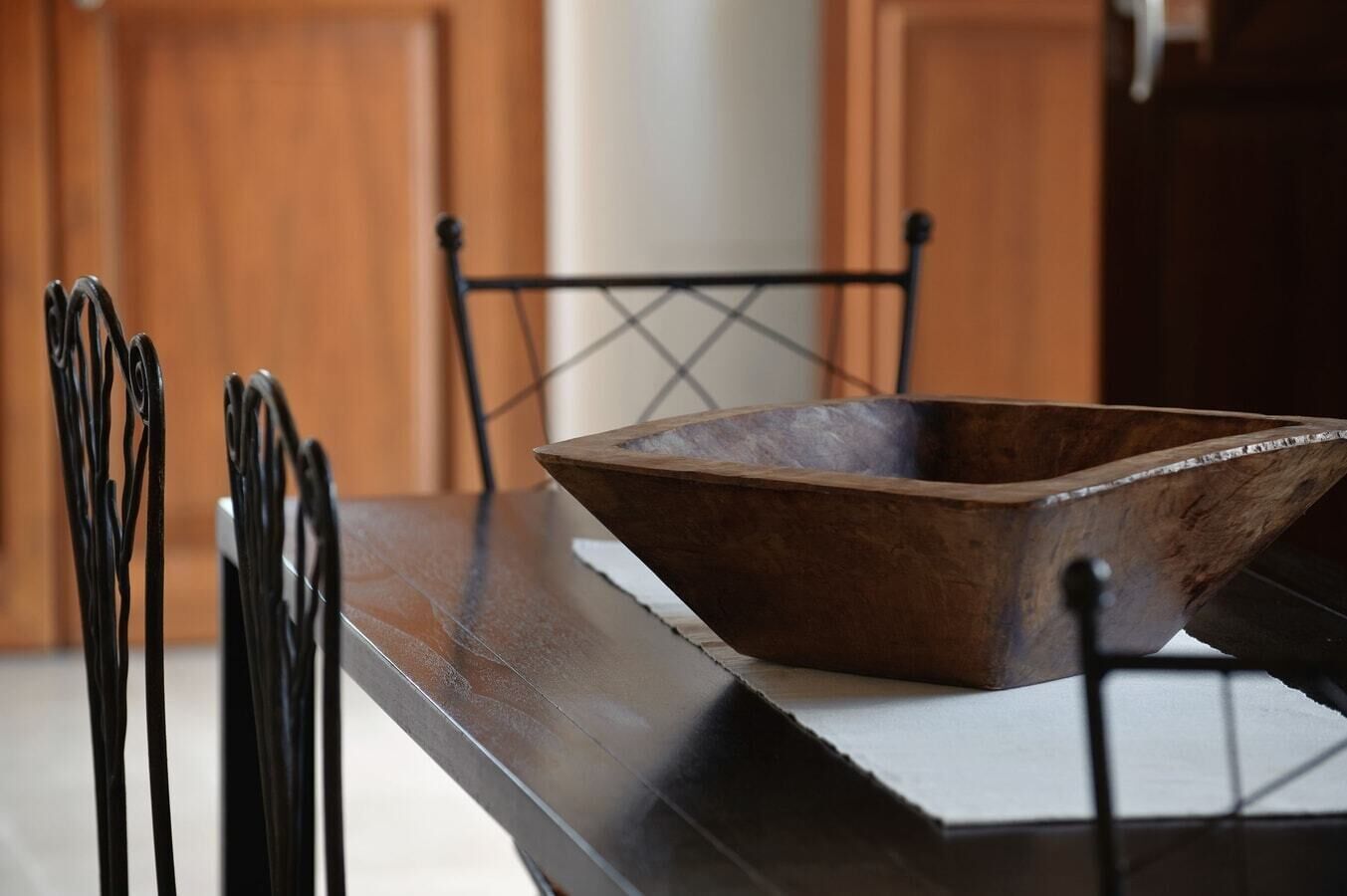 A wooden bowl on a dark countertop with metal chairs in a kitchen setting.