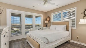 A bedroom with a bed, a ceiling fan, a nightstand, a lamp, and a window with blinds. - Panoramic views from the wrap around porch overlooking south bald head (Bald Head Island)