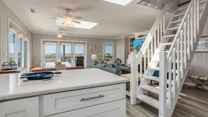 A spacious living area with a large window, a ceiling fan, and a white staircase. - Panoramic views from the wrap around porch overlooking south bald head (Bald Head Island)