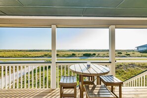 Um deck de madeira com mesa e bancos, com vista para uma paisagem gramada.