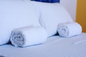 Siististi pedattu sänky, jossa on valkoiset lakanat ja rullalle taitetut pyyhkeet.