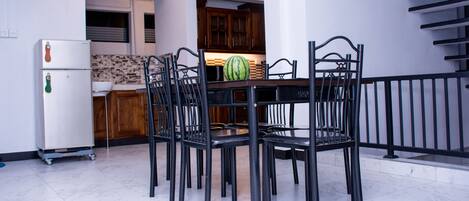 A dining area with a table and chairs, a refrigerator, and a kitchen in the background.