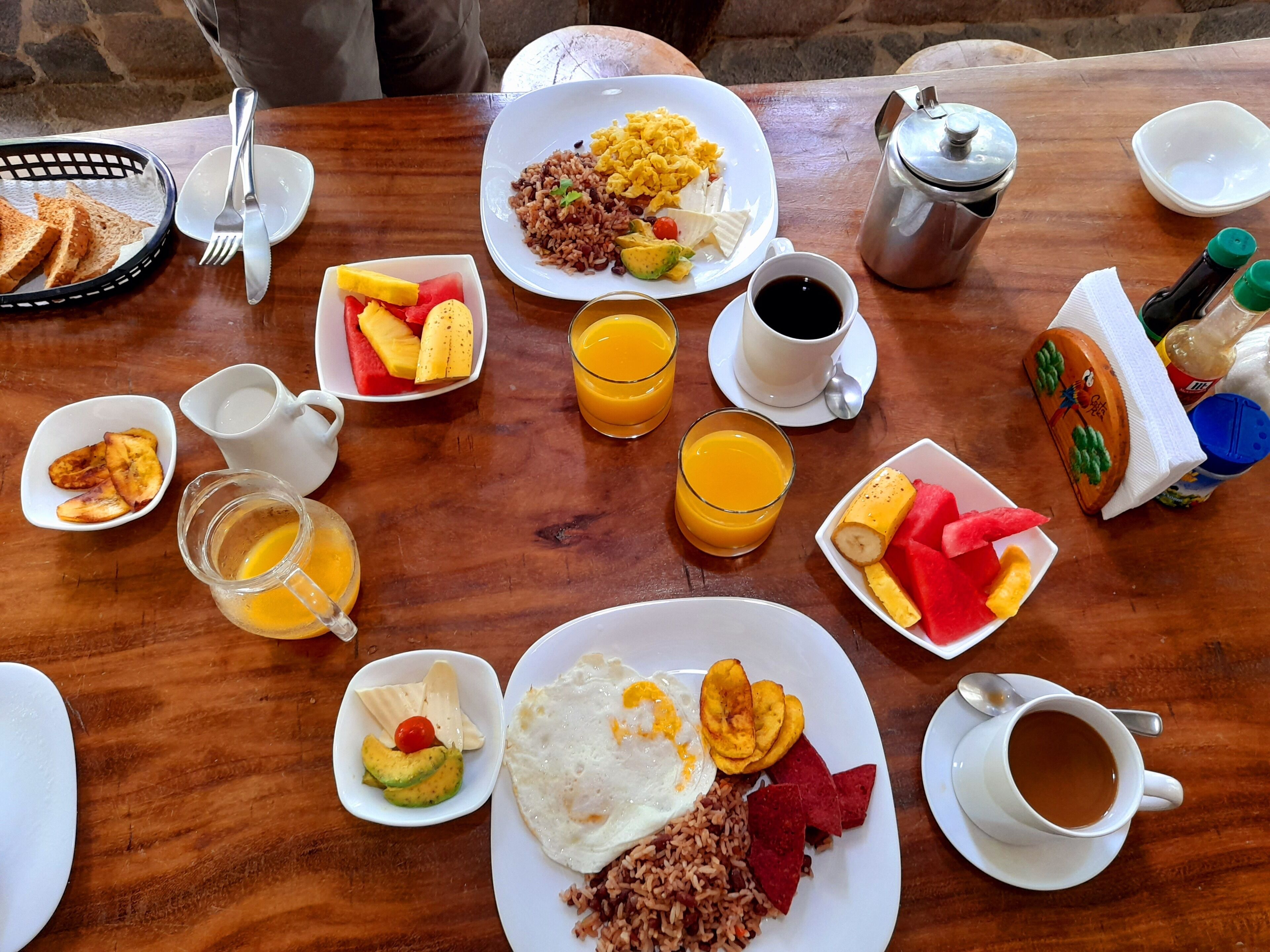 A breakfast table with plates of food, glasses of orange juice, a coffee pot, and condiments.