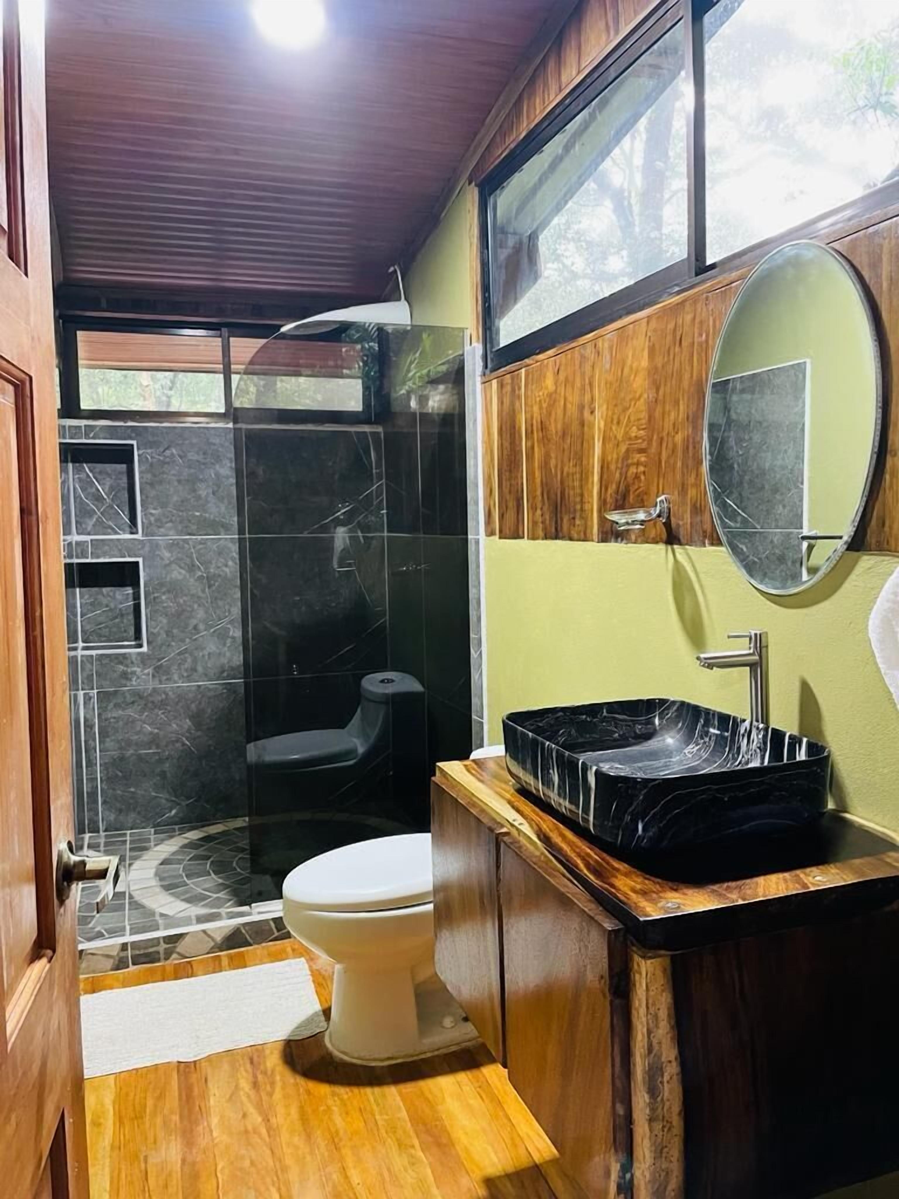 Un baño moderno con lavamanos negro, inodoro blanco y cabina de ducha de vidrio.