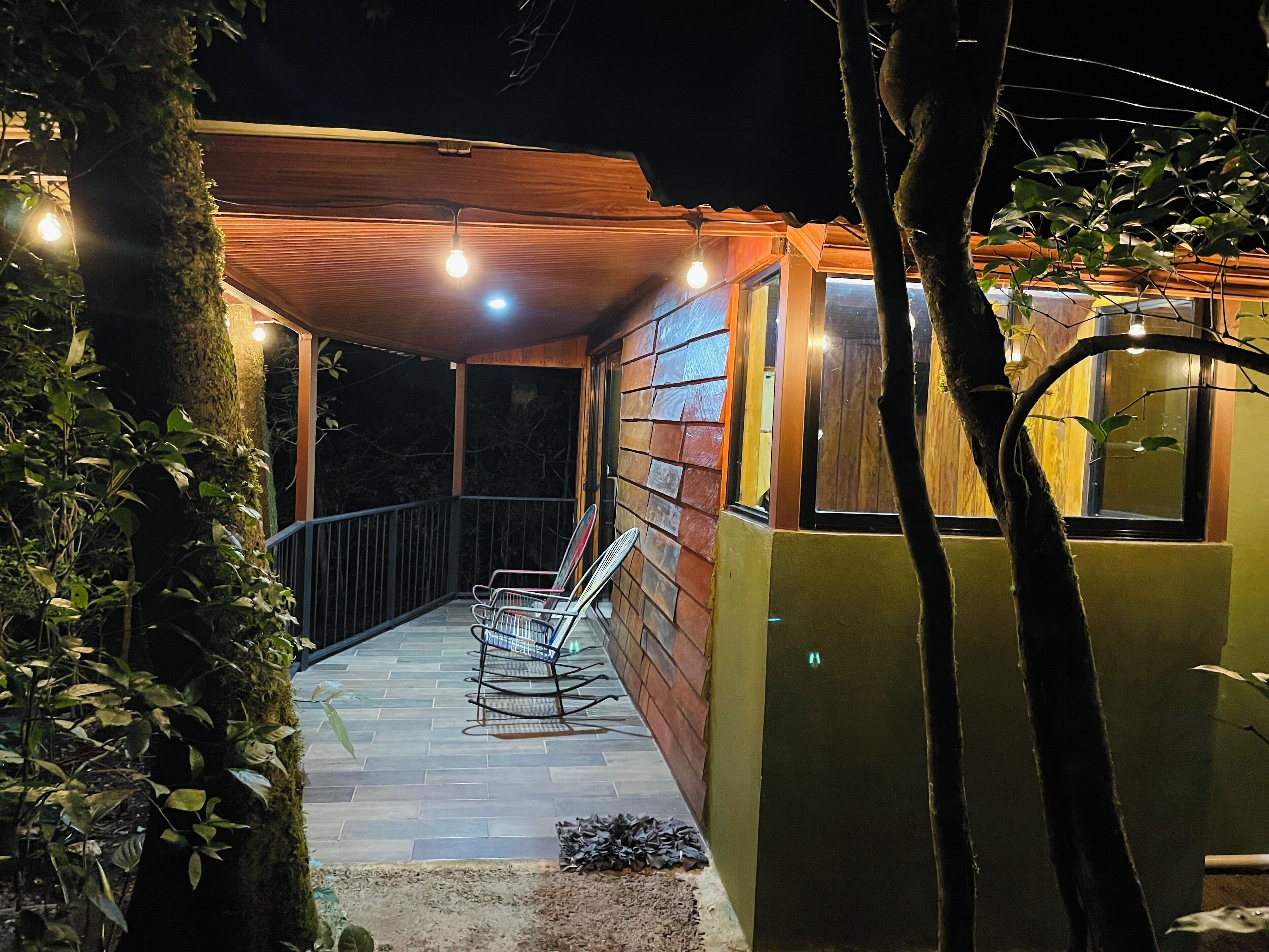 A wooden cabin with a balcony, string lights, and a rocking chair.