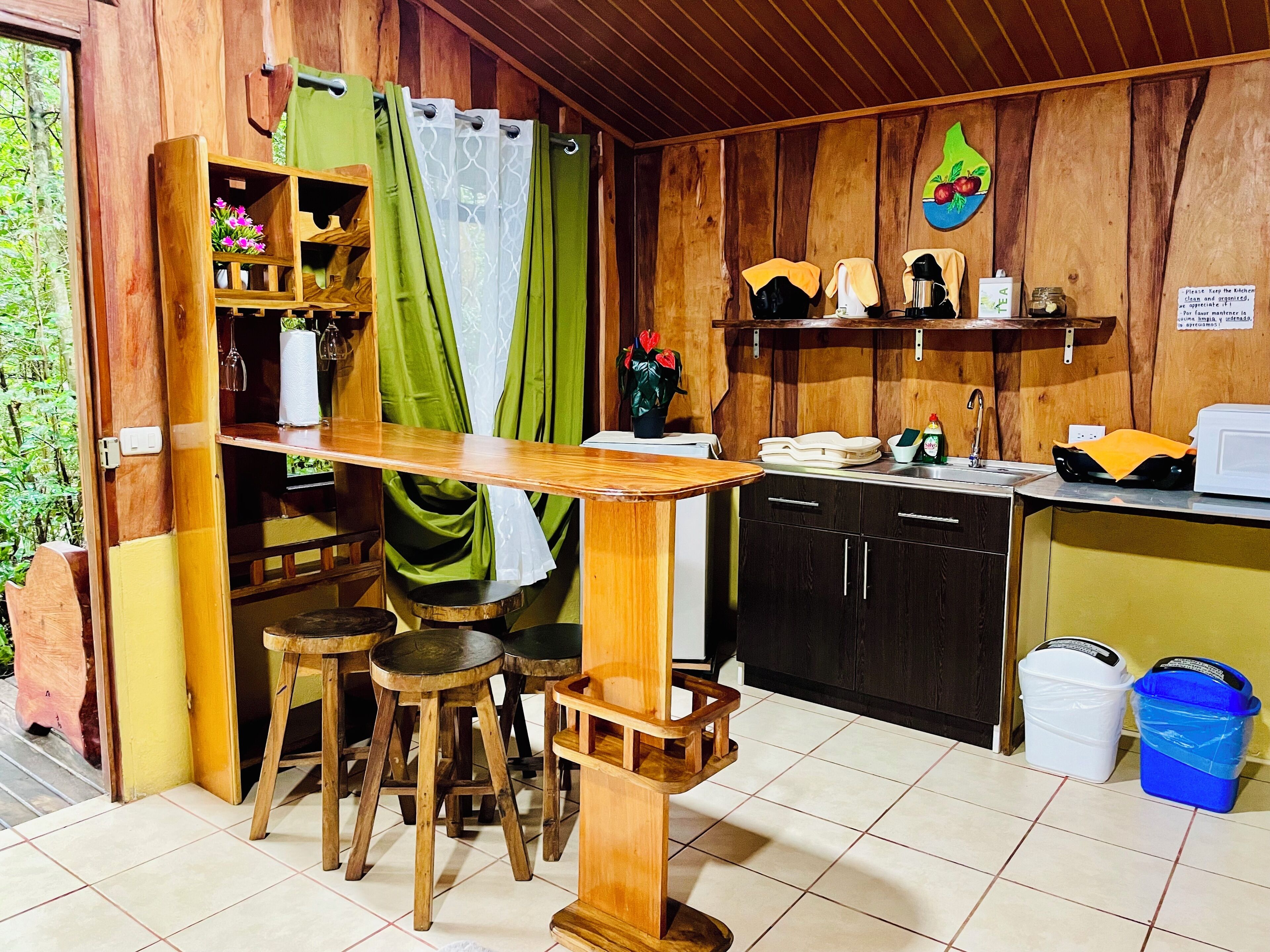 A compact kitchen with wooden cabinets, a small dining area with stools, and a green curtain.