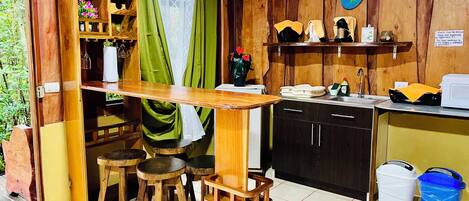 A compact kitchen with wooden cabinets, a small dining area with stools, and a green curtain.