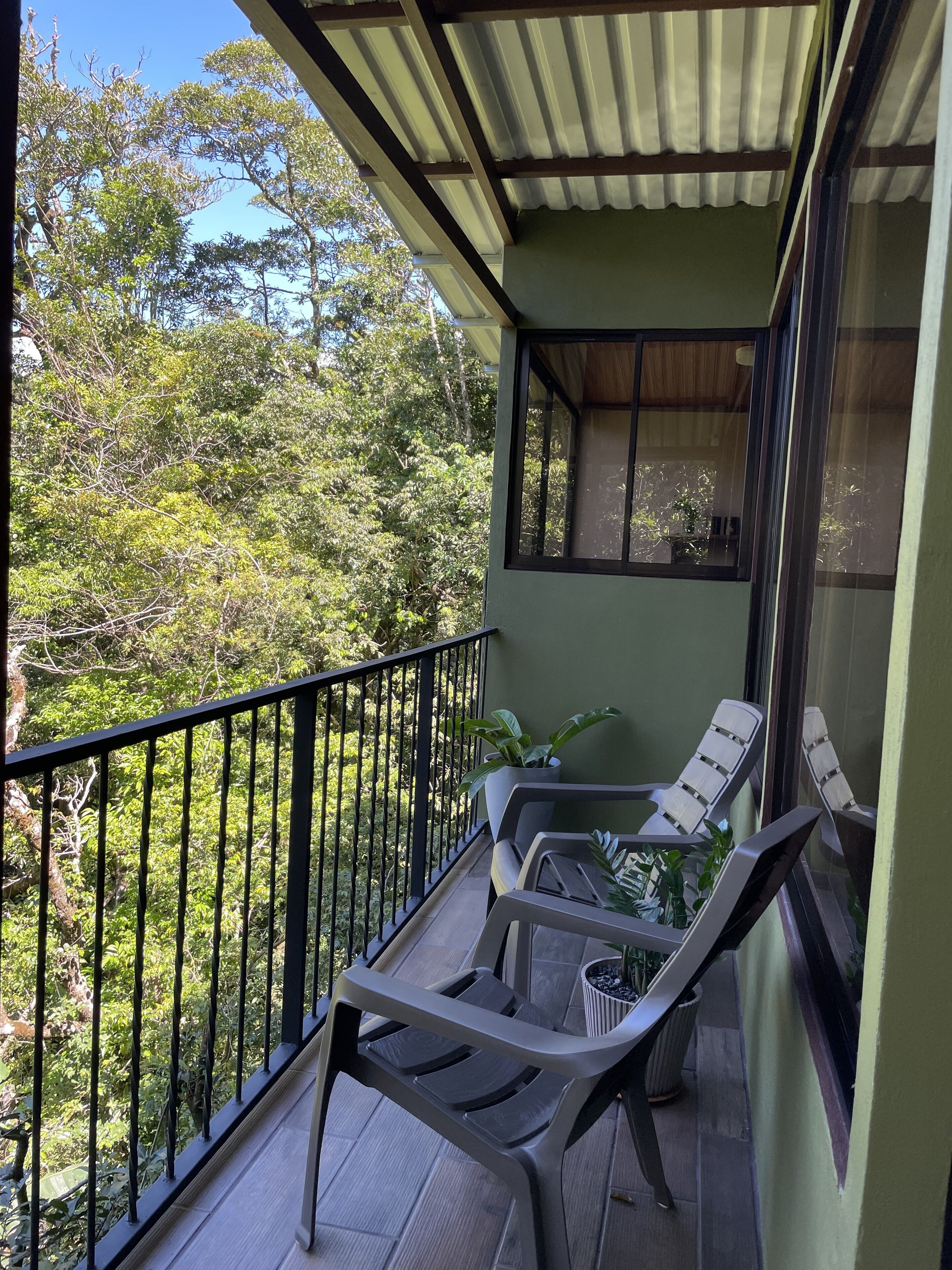 A balcony with two lounge chairs and a potted plant, overlooking a lush green landscape.