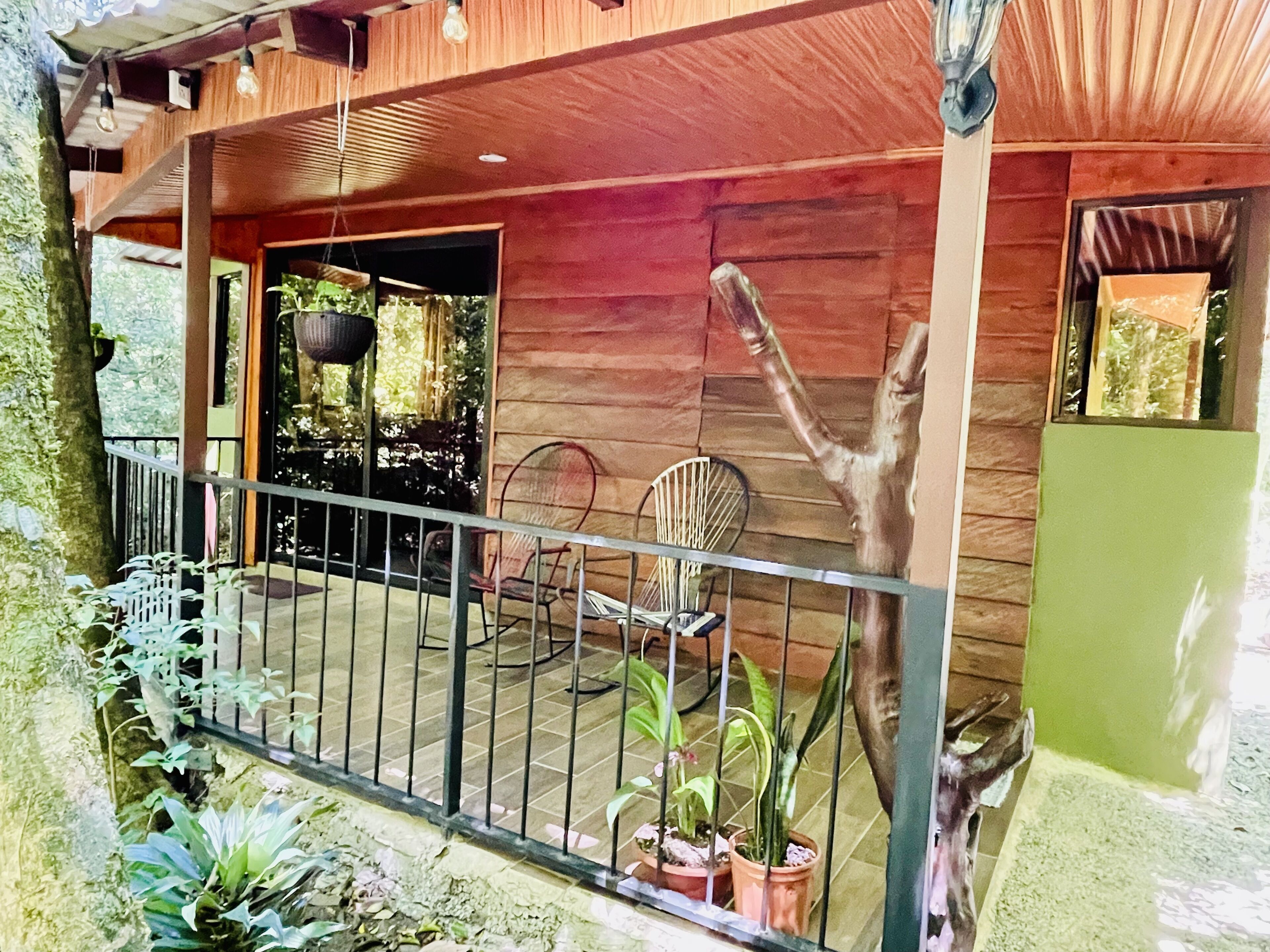 A wooden building with a covered porch, potted plants, and a metal railing.