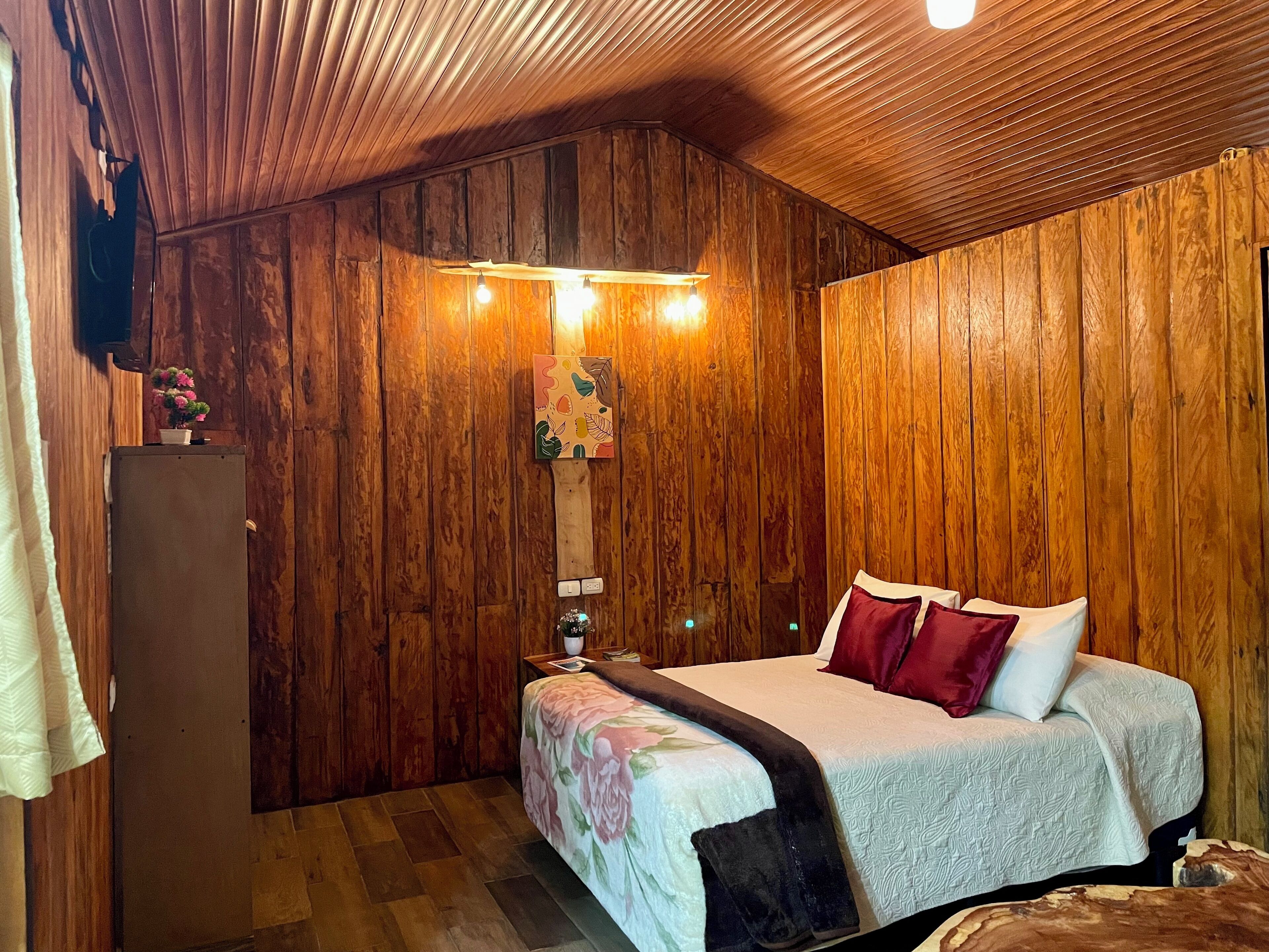 A wooden-paneled room with a bed, a nightstand, and a wall-mounted lamp.