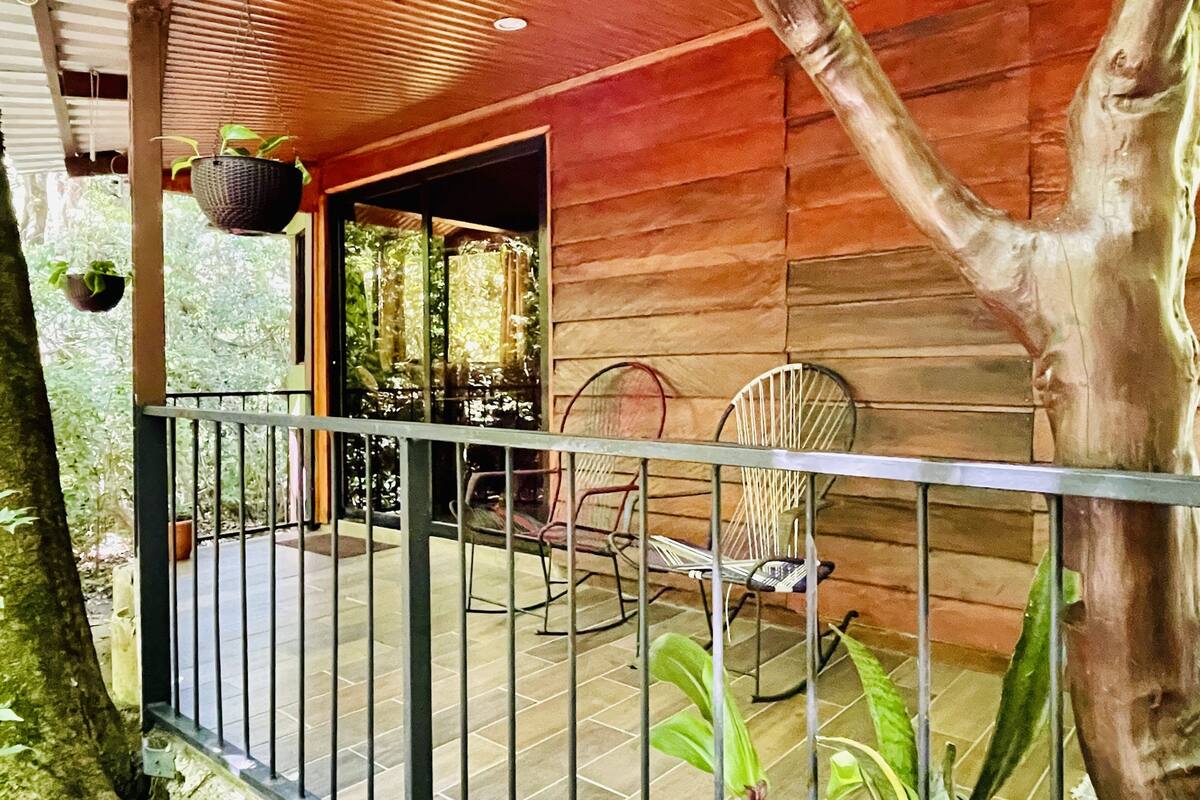 A wooden cabin with a balcony, metal railing, and two chairs.