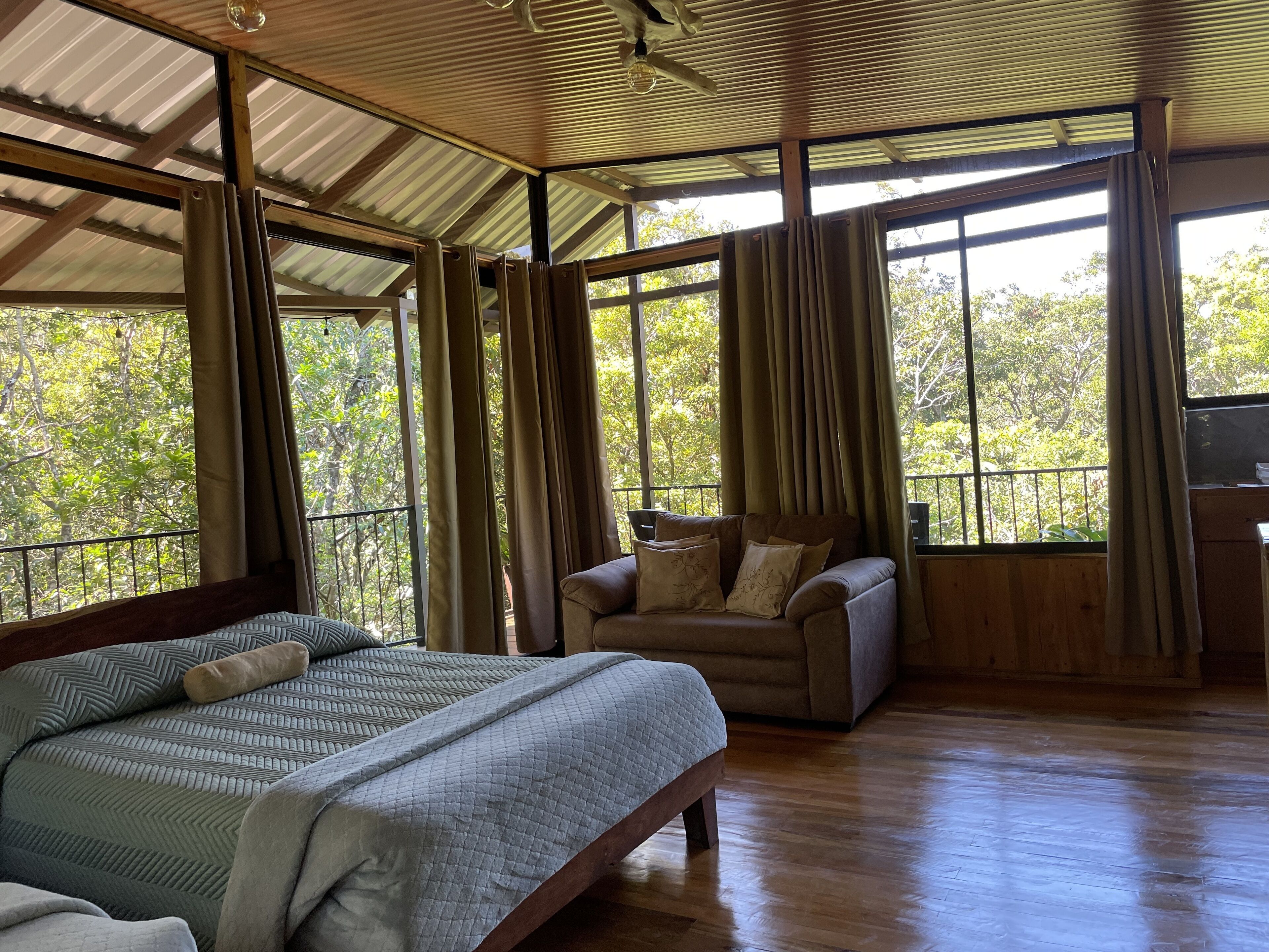 A spacious room with a large bed, a sofa, and a wooden floor.
