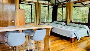 A room with a wooden ceiling, a bed, a desk with two chairs, and large windows offering a view of greenery. - Cabañas La Montaña (Monteverde)