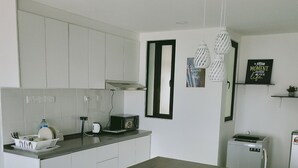 A modern kitchen with white cabinets, a stainless steel countertop, a microwave, a toaster, and a sink. There are two bar stools and a hanging light fixture. - South Key Mosaic (Johor Bahru)