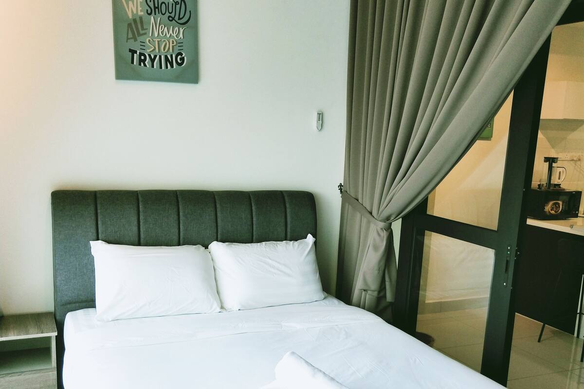 A neatly made bed with white linens, a dark headboard, and a motivational quote on the wall.