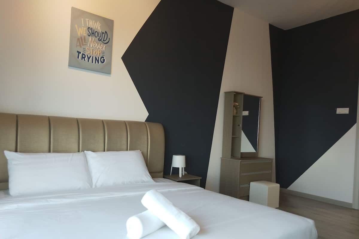 A neatly made bed with white linens, a pillow, and two rolled towels. A small bedside table with a lamp is visible. The room features a modern design with a geometric wall pattern and a large mirror.