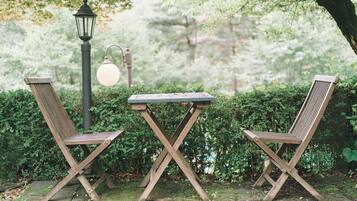 Dos sillas de madera y una mesa en un jardín, con una farola y follaje.
