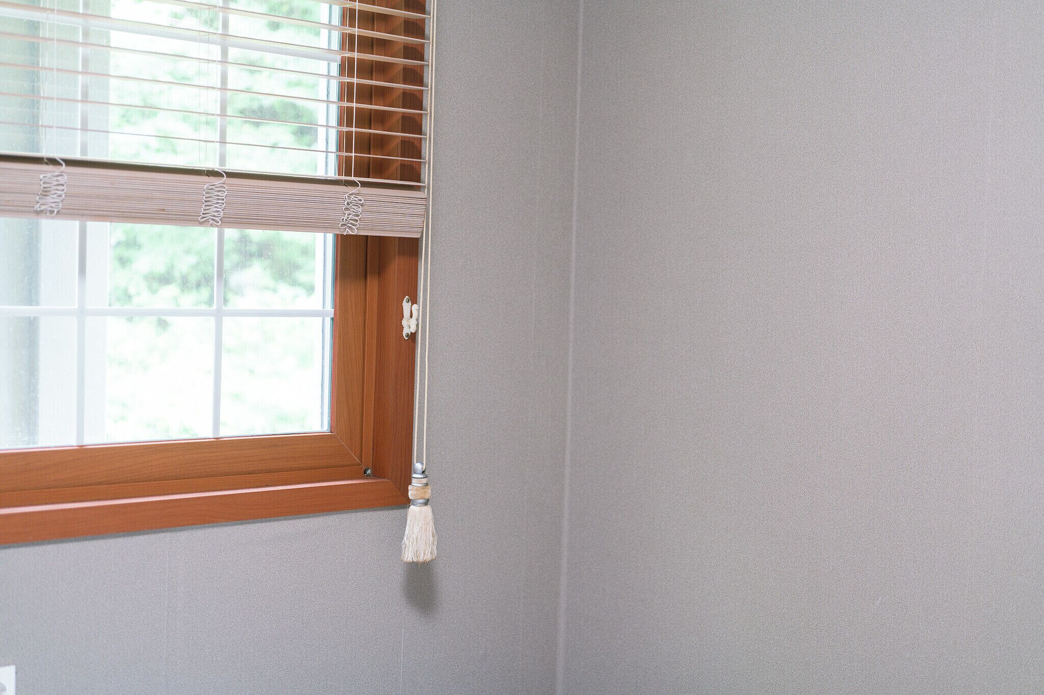 A window with a wooden frame, a white curtain, and a tassel hanging from the curtain rod.