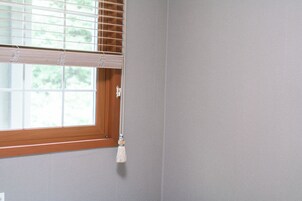 A window with a wooden frame, a white curtain, and a tassel hanging from the curtain rod.
