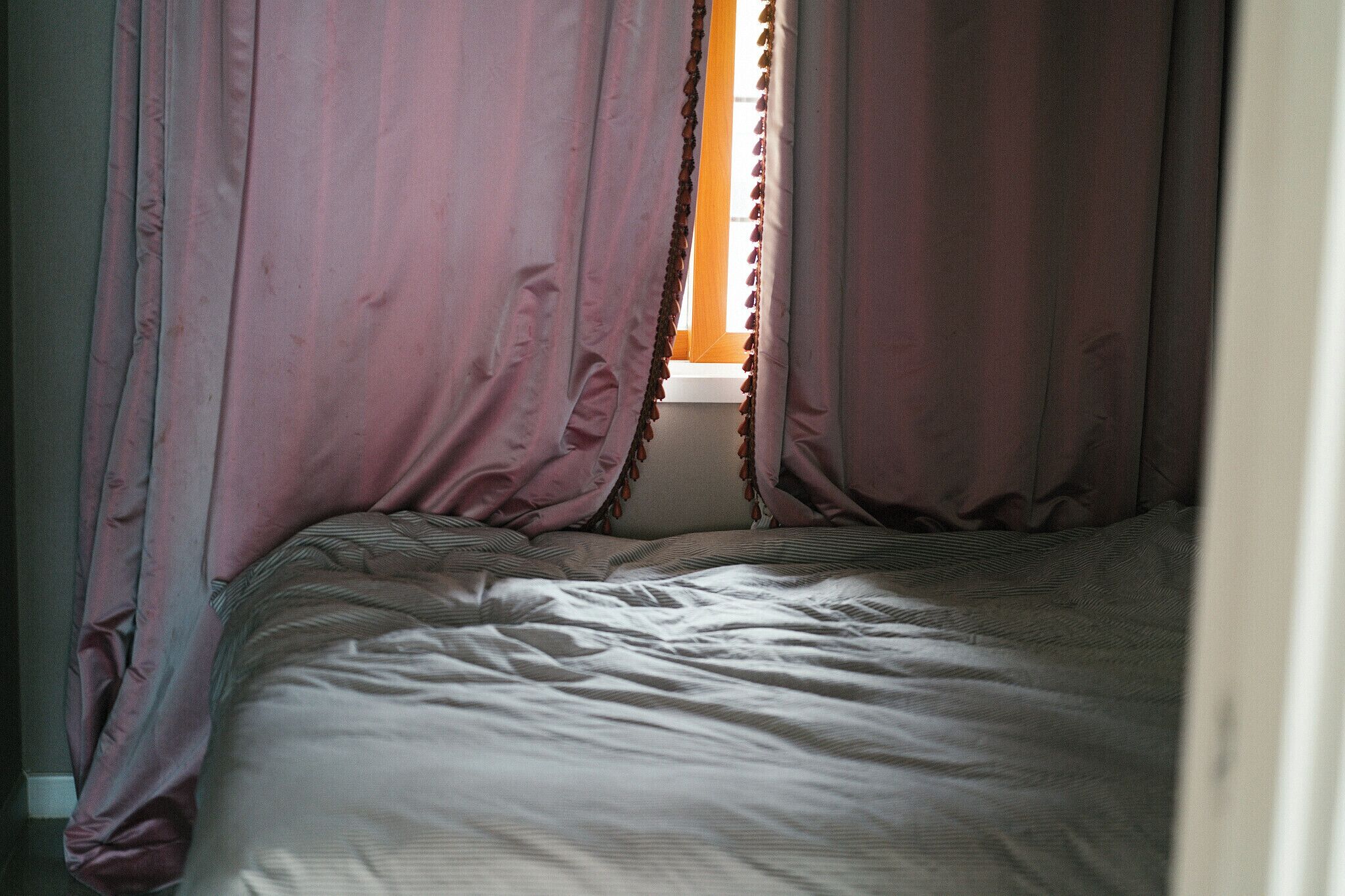 Una cama con una manta a rayas, una ventana con cortinas y una vista parcial de una pared.