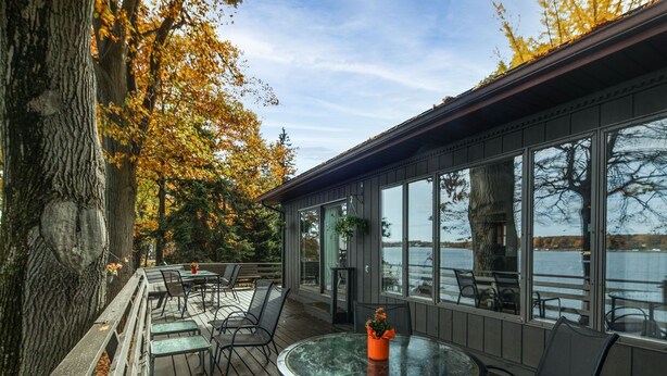 Une terrasse extérieure couverte, dotée d’une table et de chaises en verre, qui offre une vue sur une étendue d’eau.