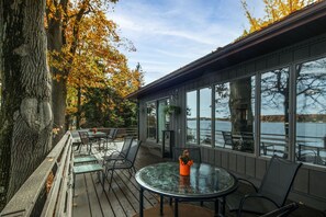 Terraza techada al aire libre con una mesa y sillas de vidrio, con vista a un cuerpo de agua.