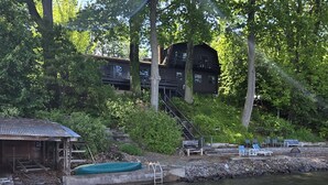 Un chalet au bord du lac, avec un petit quai, un bateau à l’abri et un escalier menant à un bâtiment.