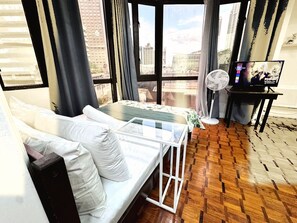 A room with a bed, a small table, a fan, and a TV. - Charming overview studio by Greenbelt (Netflix &  pool) (Legaspi Village, Makati)