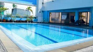 En swimmingpool med krystalklart, blå vand, omgivet af en moderne bygning med store vinduer og en blå facade.