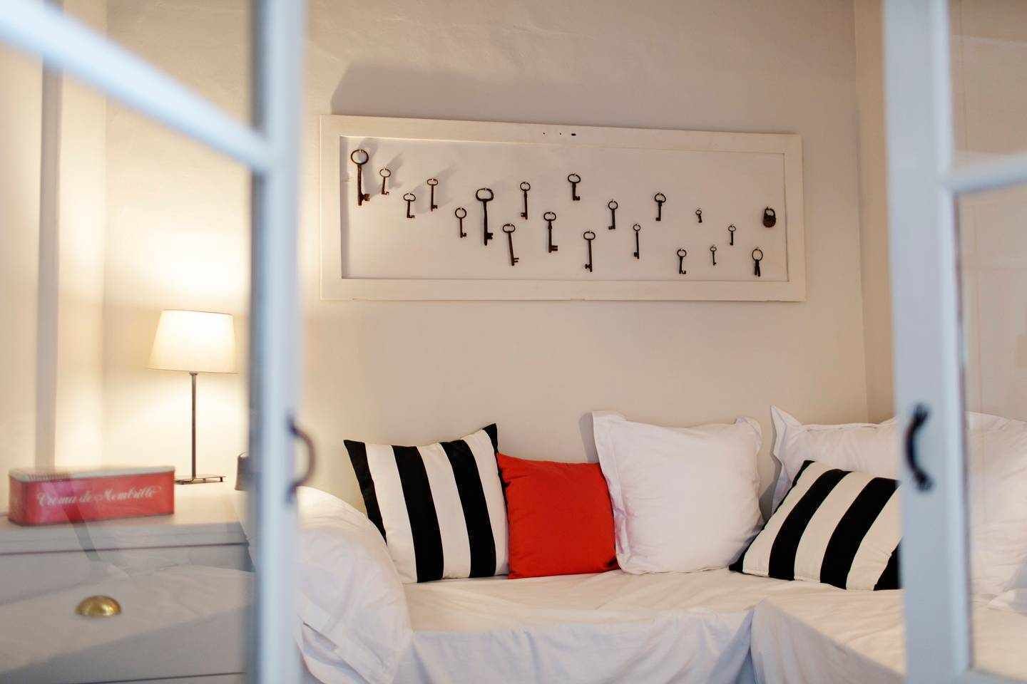 A bedroom with a bed, pillows, a nightstand, a lamp, and a wall-mounted key display.