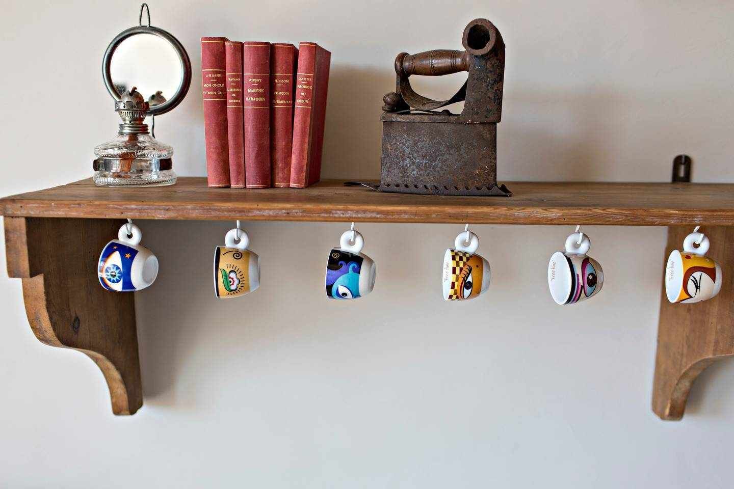 Una estantería de madera con libros, un objeto metálico y tazas.