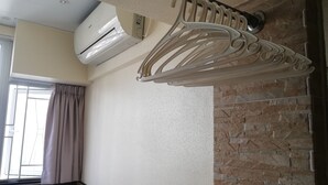 A hotel room with a bed, a window with curtains, a wall-mounted air conditioner, and a decorative metal rack. - China Guest House (Kowloon)