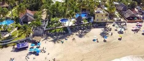 Un resort costero con acceso a la playa, palmeras y zona de piscina.