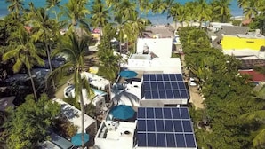 A coastal area with solar panels on rooftops, palm trees, and a view of the ocean. - Villa Robalo - Villas del Palmar (Sayulita)