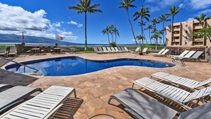 Ein Poolbereich mit Liegestühlen, Palmen und Blick auf das Meer.