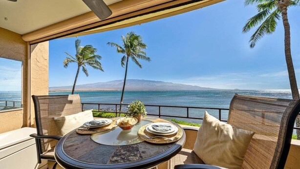 Ein Balkon mit Tisch für zwei Personen, mit Blick auf einen Strand mit Palmen und freiem Meerblick.